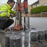 A core-drilling rig cutting a cylindrical sample from a road surface, with extracted cores on the kerb