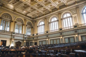 Daylight through tall arched windows onto the ornate ceiling of a legislative chamber