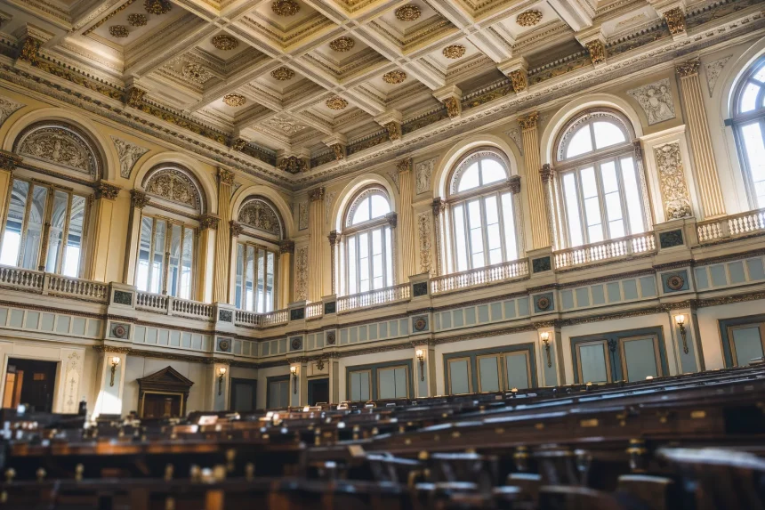 Daylight through tall arched windows onto the ornate ceiling of a legislative chamber