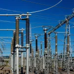 A high-voltage substation with steel lattice towers against a deep blue sky
