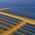 Aerial view of a large solar farm with panels in rows across golden ground
