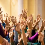Macro of many raised hands as an overlapping pattern against a sunlit wall