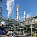 A petrochemical refinery with silver towers against a bright blue sky