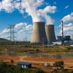 A large power station with cooling towers under a bright sky